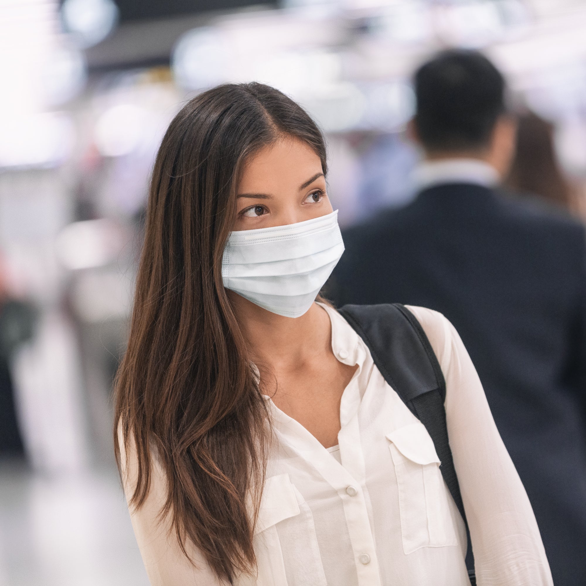 Frau mit Maske in Menschenmenge – Symbolbild für COVID-19 und virale Erkrankungen