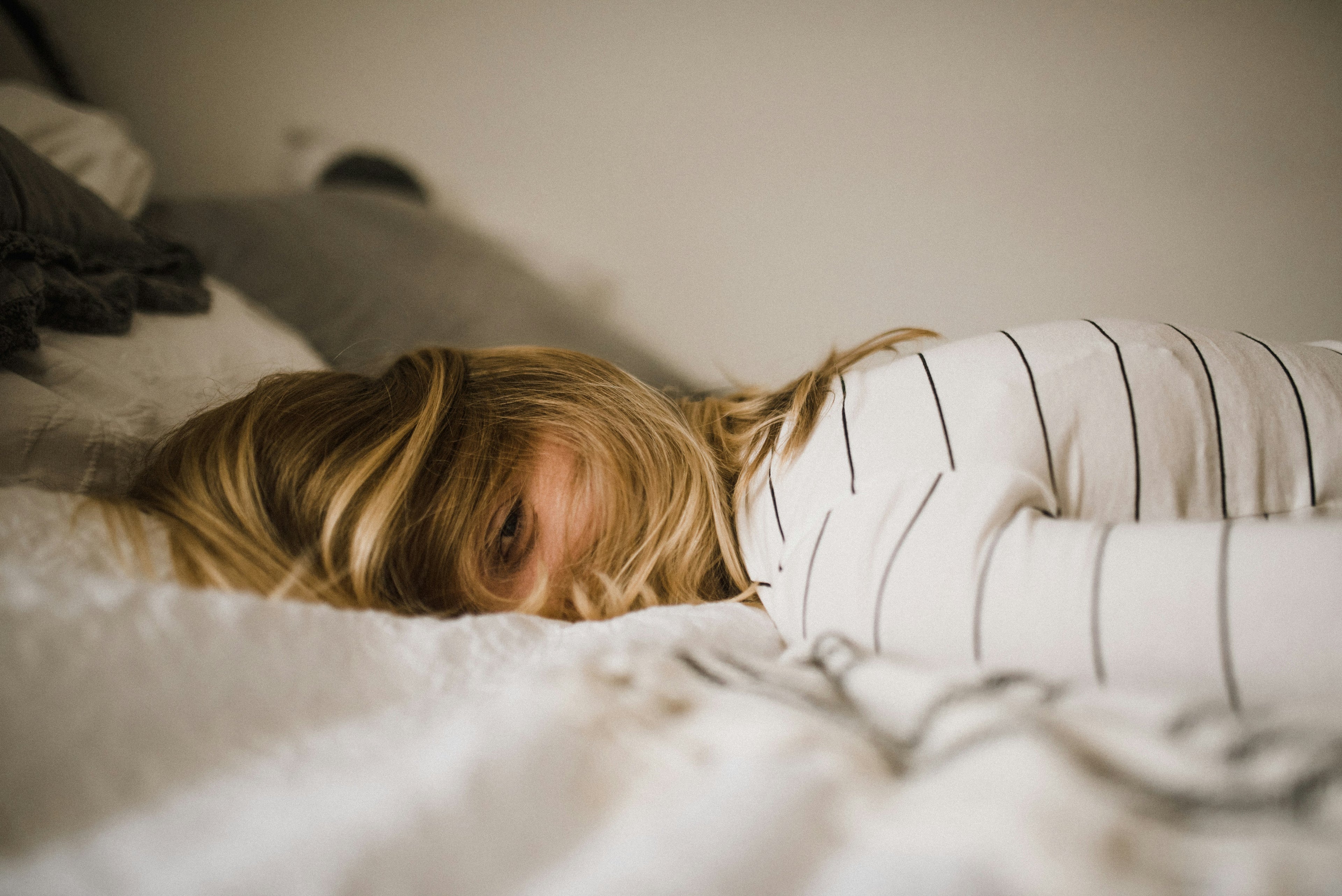 Frau liegt erschöpft im Bett – Erschöpfung und Belastung als mögliche Auslöser von Haarausfall